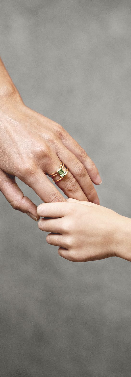 An adult's hand holding a child's hand, both wearing gold jewellery